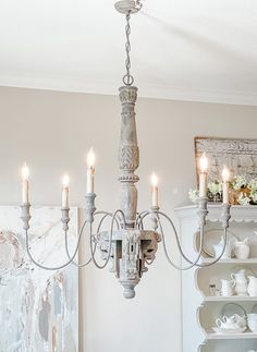 a chandelier hanging from the ceiling in a dining room with white walls and furniture