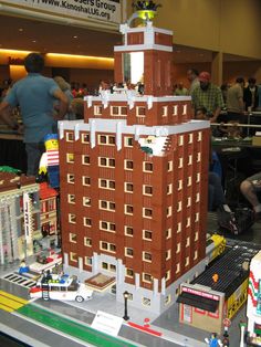 a lego model of a building with people around it and on the ground looking at other buildings