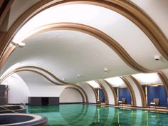 an indoor swimming pool surrounded by curved wood and glass walls, with chairs on either side