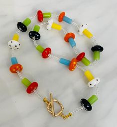 A whimsical cottagecore style inspired necklace- multicolor bright glass lamp work bead mushroom necklace. Finished with a gold toggle clasp. 17" in length. Bead Mushroom, Whimsical Cottagecore, Toadstool Mushroom, Cottagecore Mushroom, Mushroom Necklace, Style Cottage, Cottagecore Style, Toggle Necklace, Rainbow Glass