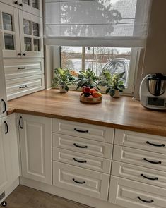 a kitchen with white cabinets and wooden counter tops next to a coffee pot on the window sill