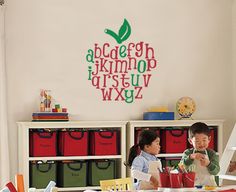 two children are sitting at a desk with an apple wall decal above the desk