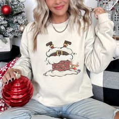 DESCRIPTION Retro Santa Going Down The Chimney Christmas Sweatshirt Celebrate the holiday season in style with this festive women's Christmas sweatshirt! Designed with a cheerful holiday theme, this cozy sweatshirt is perfect for all your seasonal activities--from decorating the tree to sipping hot cocoa by the fire. Made from soft, premium fabric, it's designed to keep you warm and comfortable while spreading holiday cheer. Whether you're attending a Christmas party, going on a holiday shopping Cozy Crew Neck Holiday Tops, Cozy Holiday Crew Neck Top, Cozy Crew Neck Top For Holidays, Casual Christmas Sweatshirt For Festive Occasion, Casual Christmas Festive Sweatshirt, Casual Christmas Sweatshirt, Cozy Crew Neck Top For Christmas, Cozy Long Sleeve Holiday Tops, Cozy Long Sleeve Christmas Tops