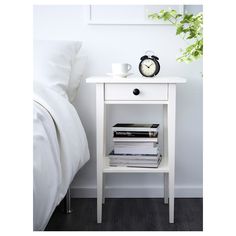 a nightstand with books and a clock on it next to a white bed in a bedroom