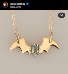 a gold necklace with two bats hanging from it's sides and a green stone in the middle