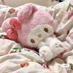 a pink and white teddy bear laying on top of a bed covered in blankets,