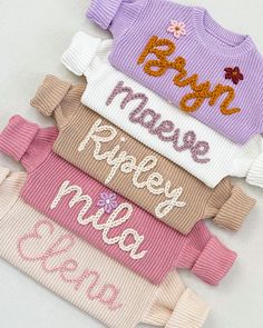 four baby sweaters are stacked on top of each other, with the names and numbers printed on them