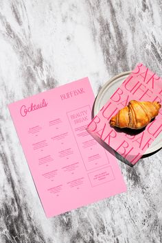 a pink menu and croissant on a plate