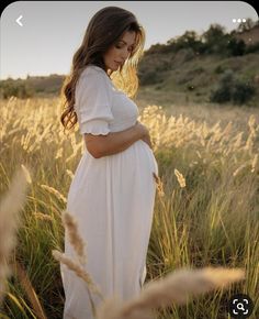 a pregnant woman standing in tall grass with her hands on her stomach, looking down