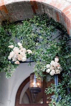 flowers are growing on the side of an arched door with wrought iron bars and brick walls