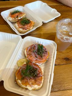 three plastic trays filled with food on top of a wooden table next to a drink