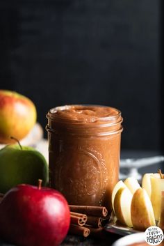 an apple pie in a jar surrounded by sliced apples and cinnamon on a table top