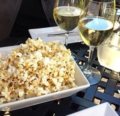 two glasses of wine and a bowl of popcorn on a table with some food in it