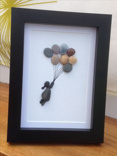 a black frame with rocks in the shape of a person holding balloons