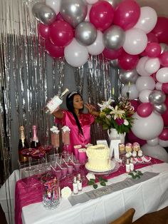 a woman standing in front of a table filled with cake and balloons