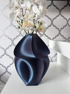 a blue vase with flowers in it sitting on a white table next to a wall