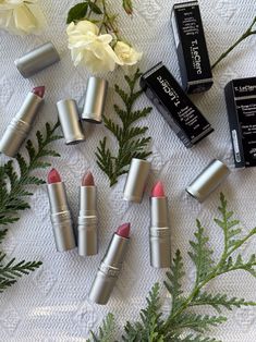 various lipsticks are arranged on a table with flowers and greenery in the background