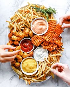 two hands reaching for dipping sauce on top of a platter of fries