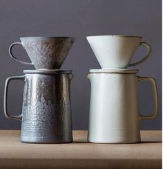 three coffee cups sitting on top of a table next to each other, one white and one gray