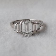 a three stone diamond ring on a white surface with the center setting surrounded by smaller baguettes