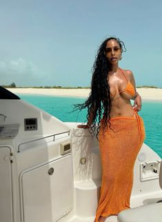 a beautiful woman in an orange dress standing on the back of a boat near the ocean