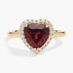 a heart shaped ring with diamonds around the band and a red stone surrounded by white stones