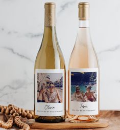 two bottles of wine sitting next to each other on a wooden board with shells around them