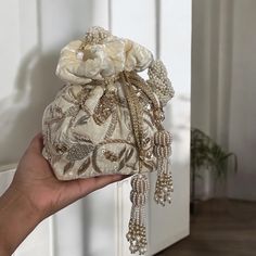 Add a touch of elegance and sophistication to your bridal look with our exquisite Cream Velvet Potli Bag. Crafted from premium velvet, this potli bag is a testament to timeless beauty and unmatched craftsmanship. The soft cream shade exudes a subtle charm that complements any bridal attire, while the intricate hand-embroidered zardozi and sequins work create a mesmerizing display of artistry. Each stitch and sequin is meticulously placed, showcasing the skill and dedication of our artisans. Designed for comfort and style, this potli bag features a stunning handmade braided handle adorned with delicate beads, offering both durability and a unique aesthetic. The handle is carefully crafted to ensure a comfortable grip, making it an ideal accessory for the bride on her special day. To further Elegant Handheld Beaded Evening Bag, Elegant Silver Embroidered Bags, Elegant Cream Bag With Pearl Handle, Luxury Beaded Potli Bag For Parties, Luxury Bag With Pearl Embroidery For Reception, Beaded Potli Bag Pouch For Gifts, Beaded Potli Bag Gift, Beaded Potli Bag Gift Pouch, Beaded Pouch Potli Bag As Gift