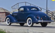 an old blue car is parked on the street in front of some stairs and buildings