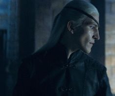 a man with long white hair wearing a black leather jacket and headband in a dimly lit room