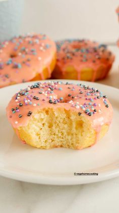 two glazed donuts with pink glaze and sprinkles on a white plate