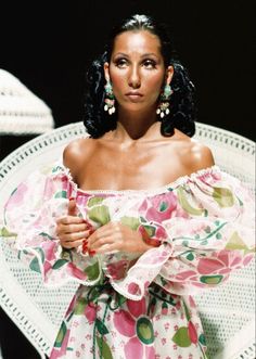 a woman in a floral dress sitting on a white chair with her arms folded up