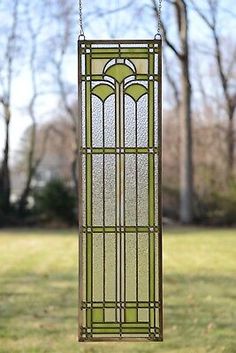 an old stained glass window hanging from a chain in front of some grass and trees