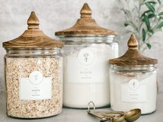 three jars filled with oats and two spoons next to each other on a table