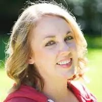 a woman with blonde hair wearing a red jacket and smiling at the camera while standing in a field