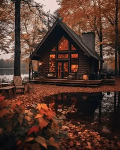 a log cabin sits on the shore of a lake surrounded by autumn leaves and trees