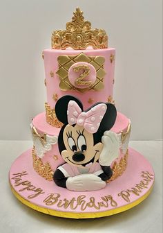 a pink and gold birthday cake with minnie mouse on top