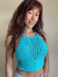 a woman wearing a blue crochet top smiling at the camera with her hair blowing in the wind