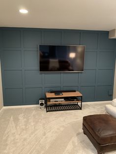 a flat screen tv mounted to the side of a wall in a living room next to a footstool