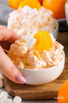 a person is holding an orange and marshmallow ice cream in a white bowl