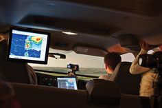 two men in the back seat of a car looking at a map on a computer screen