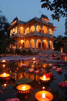 many lit candles in front of a large building with water lillies on the ground