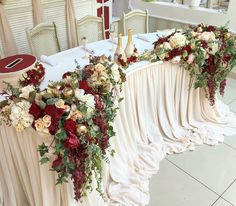 the table is decorated with red and white flowers, greenery and candles on it