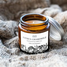 a jar of citrus chamomile sitting on top of a bed next to a candle