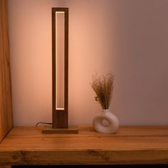 a wooden table with a white vase on it and a light in the corner next to it