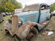 an old blue truck sitting on top of a grass covered field next to other junk