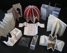 an assortment of folded and folded books on a black table with one open book in the middle