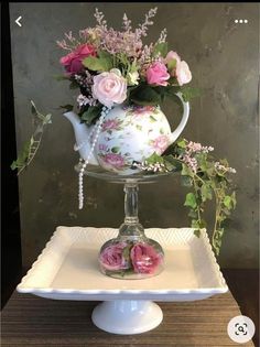 a white tea pot with pink flowers in it sitting on a tray next to a flower arrangement