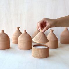 a person is arranging wooden vases on a white tableclothed surface, with one hand reaching for the top