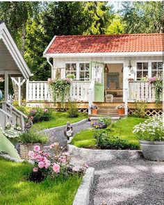 a small white house surrounded by lush green grass and pink flowers in the front yard